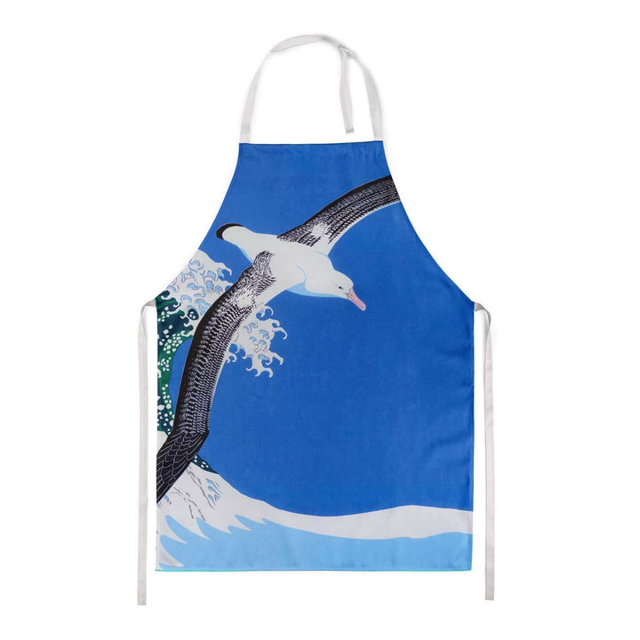 An albatross flying with a blue sky and a huge wave in the background