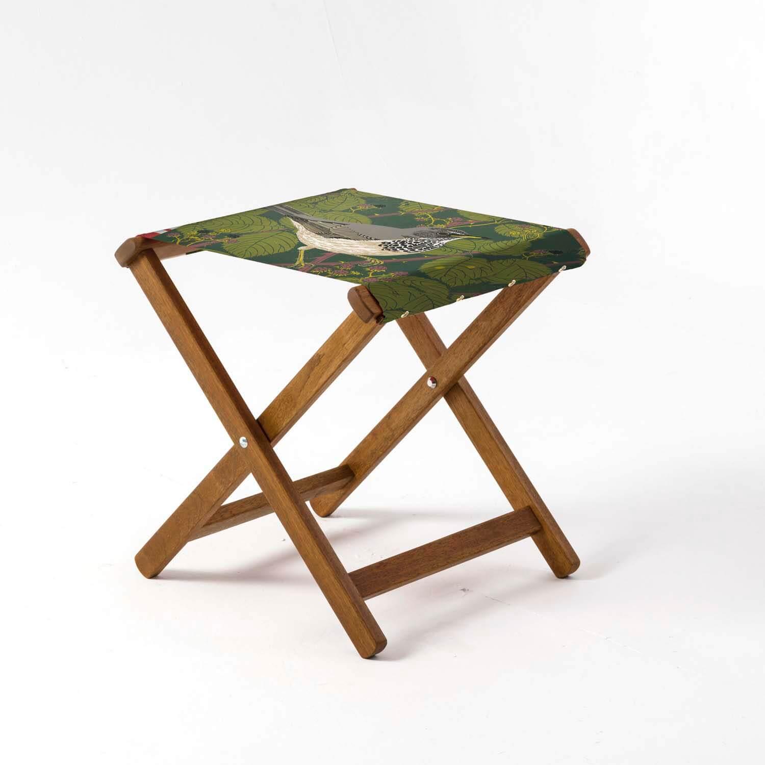 A folding wooden stool with a green fabric seat featuring a grey and white thrush.