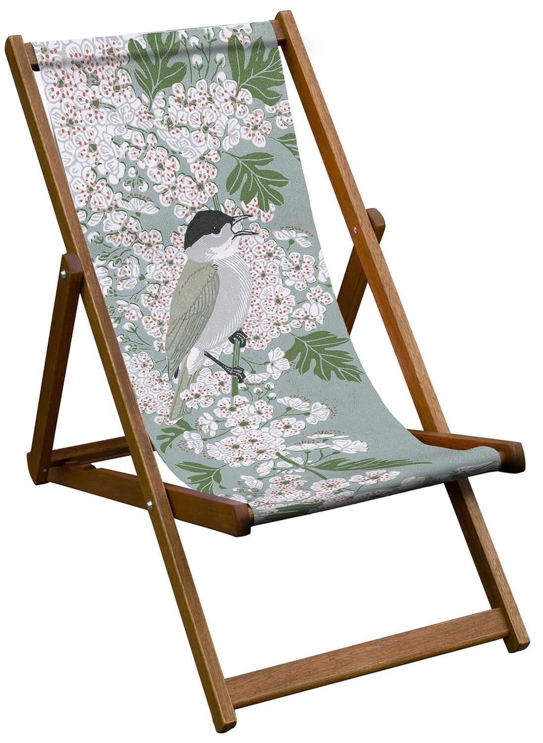 A wooden deckchair with a fabric sling. The sling has pretty white flowers and a singing bird.