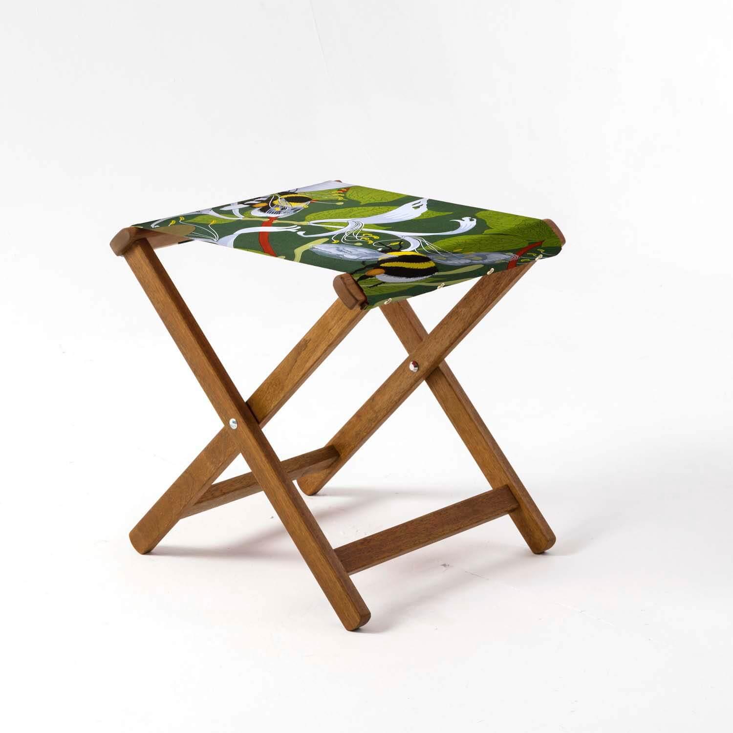 A folding wooden stool with a fabric seat. The seat shows bumble bees, white flowers and leaves on.