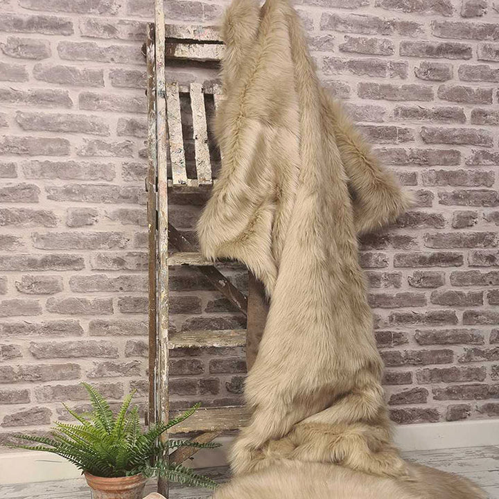 Large camel faux fur throw in light beige oatmeal hung from a decorative wooden ladder