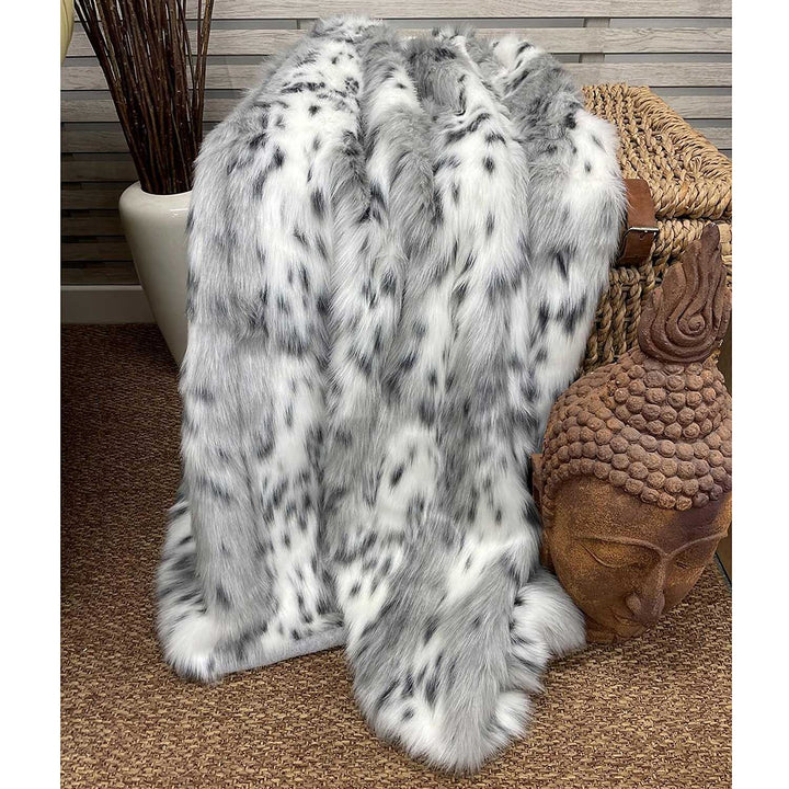 Silver gray and white faux fur throw blanket draped over a basket with decorative items in the background.