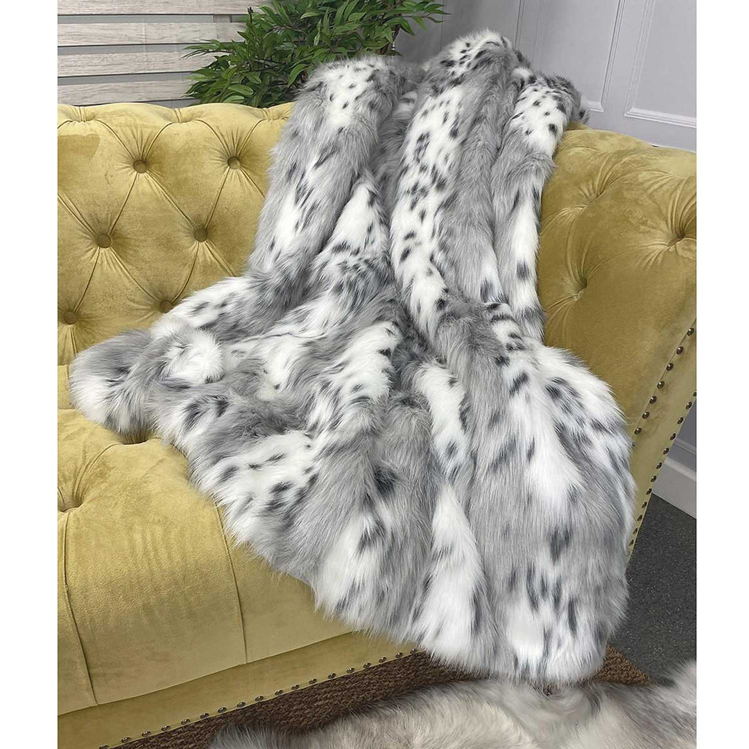 Silver gray and white faux fur throw draped over a mustard yellow button back sofa.